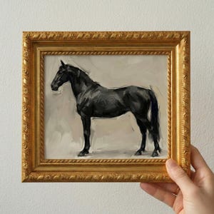 May include: A framed painting of a black horse in a gold ornate frame. The horse is depicted in profile against a light background. The frame has a detailed, textured design.