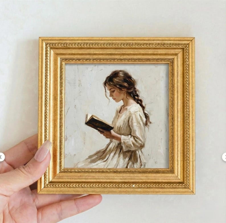 May include: A small, square, gold-framed painting depicts a woman reading a book. The woman is wearing a light-colored dress and has long, braided brown hair. The painting has a soft, muted color palette and a classical style.
