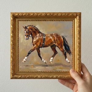 May include: Oil painting of a brown horse in a gold frame. The horse is in motion, wearing a bridle and harness. The artwork has a textured appearance, with visible brushstrokes. The frame has an ornate, detailed design.