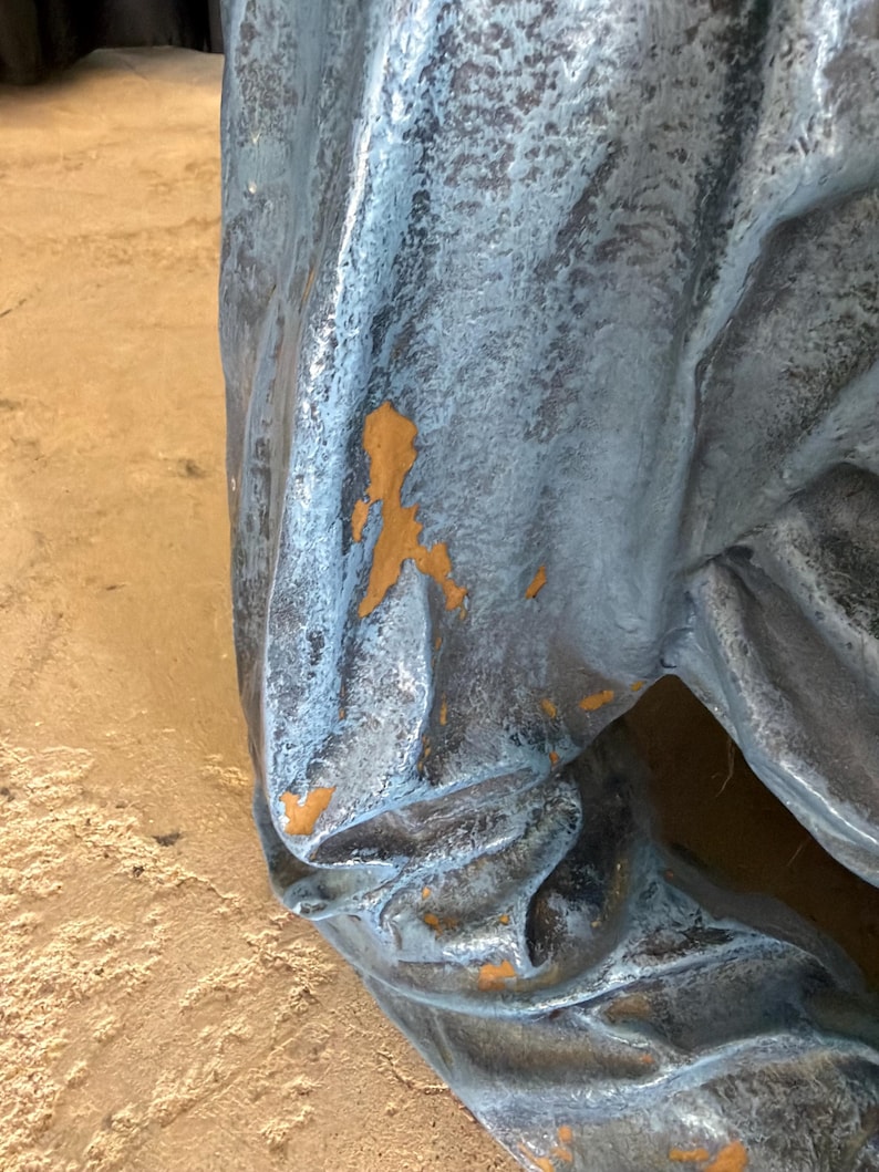 May include: A sculptural object with a textured, metallic blue-grey finish featuring deep folds and creases. The surface shows areas of wear where the blue-grey paint has chipped away to reveal a warm, mustard-yellow base layer underneath.