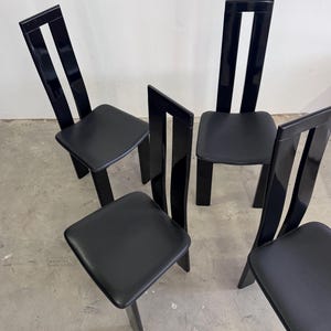 Peut inclure: Quatre chaises noires avec des assises carrées et des dossiers hauts et élégants. Les dossiers présentent un design vertical avec une découpe centrale. Les chaises ont une finition brillante.