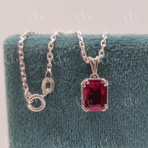 Puede incluir: Un collar de cadena de plata con un colgante que presenta una piedra preciosa grande, de forma cuadrada, de color rojo intenso.