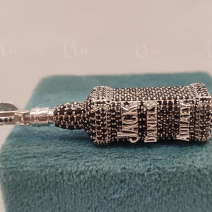 May include: A silver pendant shaped like a Jack Daniel's bottle, encrusted with black cubic zirconia stones. The words "Jack Daniels" are visible on the bottle.
