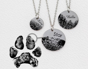 Op de afbeelding: Drie zilveren kettingen met ronde hangers met zwarte potafdrukken en gepersonaliseerde namen: "Lucy", "Star" en "Bella".