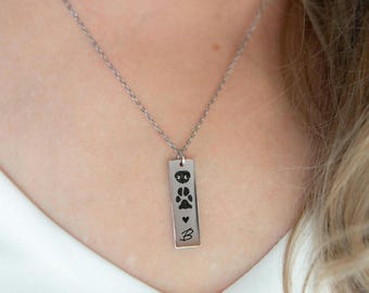 Op de afbeelding: Een zilveren ketting met een rechthoekige hanger met poot afdrukken en een hart. De hanger is gegraveerd met de letter "B".