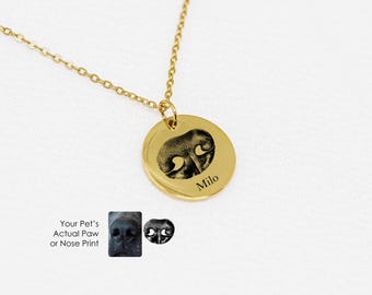 Puede incluir: Collar de oro con un colgante redondo que presenta una huella de pata en blanco y negro y el nombre "Milo" grabado en él. El texto "Your Pet's Actual Paw or Nose Print" también está incluido en la imagen.