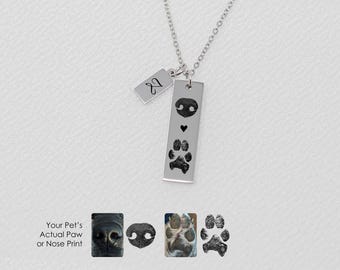 May include: Silver necklace with a small charm that says "2" and a larger charm with a paw print and a heart. The larger charm is engraved with a paw print and a heart. The necklace is on a white background.