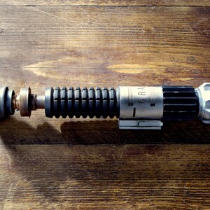 Peut inclure: Un accessoire de sabre laser noir et argent avec une poign&eacute;e noire textur&eacute;e et un canon argent&eacute; avec le mot "GRAH" imprim&eacute; dessus.