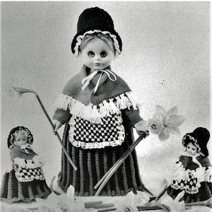 May include: Three crocheted dolls dressed in traditional Welsh costumes. The dolls are wearing black hats, white aprons, and red shawls. The dolls are holding daffodils and sticks.