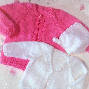May include: Two knitted baby cardigans, one pink and one white, with button closures. The cardigans have a delicate lace pattern.