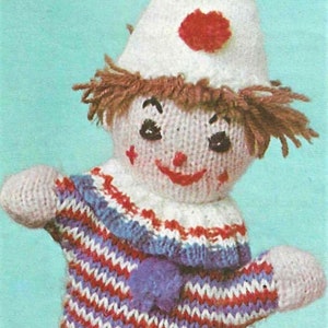 May include: A knitted clown puppet with a white hat, red and blue pom-poms, and a striped sweater. The puppet has a smiling face with red lips and black eyes.