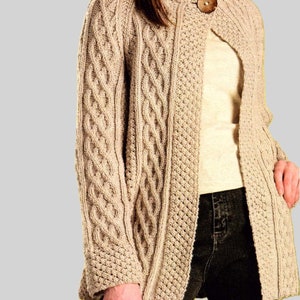 May include: A beige knitted cardigan with a cable knit pattern and a single button closure. The cardigan is worn over a white t-shirt and dark blue jeans.