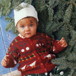 May include: A baby wearing a red and white knitted cardigan with a festive design. The cardigan has a button closure and is decorated with white birds, red cherries, and green leaves. The baby is also wearing a white knitted hat.