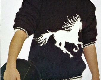 May include: A young person wearing a black sweater with a white horse design. The sweater has a white trim around the neckline and cuffs. The person is holding a black riding helmet with the number "5" on it.