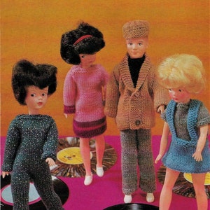 May include: Four dolls wearing knitted clothing stand on vintage vinyl records. The dolls are wearing a pink sweater dress, a blue dress, a brown sweater jacket and pants, and a blue sweater jumpsuit. The dolls are all standing on black vinyl records with yellow labels.