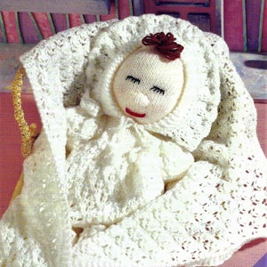 May include: A white crocheted baby doll with a red flower on its head, lying in a white crocheted blanket. The doll is in a wicker basket with a gold trim. The text "Isn't she adorable!" is written on a purple background.
