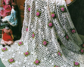 May include: A white crocheted tablecloth with a delicate floral pattern. The tablecloth features a repeating design of small pink and green flowers. The tablecloth is draped over a wooden table with a white pitcher and bowl on top.