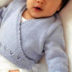 May include: A light blue baby cardigan with a wrap style and a delicate lace pattern. The cardigan is tied with a white ribbon.