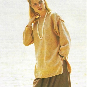 May include: A woman wearing a light brown sweater with a pearl necklace and a brown skirt.
