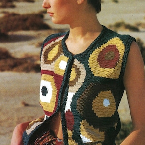 Peut inclure: Un gilet sans manches à boutons avec un motif de crochet géométrique coloré. Le gilet présente une base vert foncé avec des motifs circulaires et carrés jaunes, marron, blancs et rouges. Le gilet est porté sur une chemise à motifs et un jean bleu.