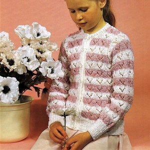 May include: A young girl wearing a pink and white striped knitted cardigan with a button fastening. She is holding a white flower and looking down at it.