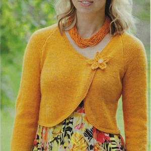 May include: A yellow knitted cardigan with a flower detail on the front. The cardigan is worn over a floral print dress.