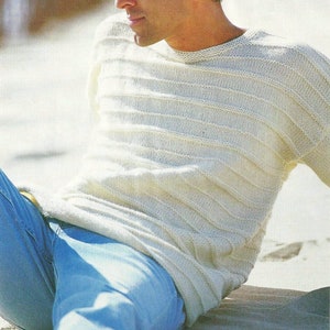 Peut inclure: Un pull en tricot blanc à rayures horizontales. Le pull a un col rond et des manches longues. Le modèle porte un jean bleu.