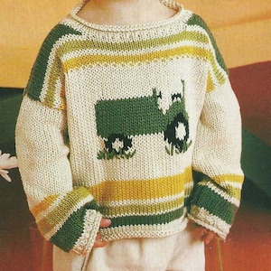 May include: A white knitted sweater with green and yellow stripes and a green tractor design. The sweater has a round neckline and long sleeves.