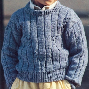 Può includere: Un maglione blu lavorato a maglia con un motivo a treccia. Il maglione ha un collo rotondo e maniche lunghe.