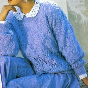 May include: A woman wearing a light blue knitted sweater with a lacy pattern. She is also wearing a white lace collar and has her hair in a braid.