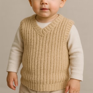 Puede incluir: Un bebé con un chaleco de punto acanalado color beige sobre una camisa de manga larga color crema. El chaleco tiene cuello en V y un patrón de canalé vertical. El bebé mira directamente a la cámara.