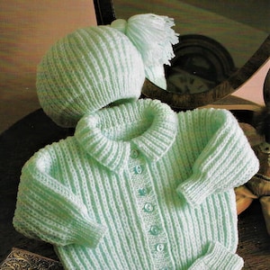 May include: A light blue knitted baby cardigan with a matching hat and mittens. The cardigan has a button closure and a ribbed texture.
