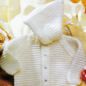 May include: A white, knitted baby cardigan and matching bonnet set. The set features a textured, horizontal ribbing pattern and is fastened with three small, round buttons. The bonnet has a rounded shape, and the set is made of a soft, light-colored yarn.
