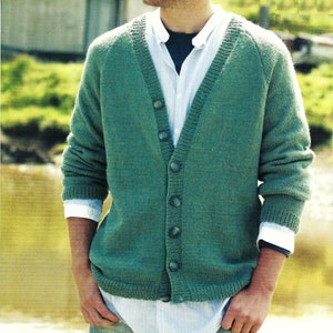 May include: A green knitted cardigan with a V-neck and button closure. The cardigan is worn over a white collared shirt and a dark blue undershirt. The sleeves are long, and the person is wearing blue jeans.