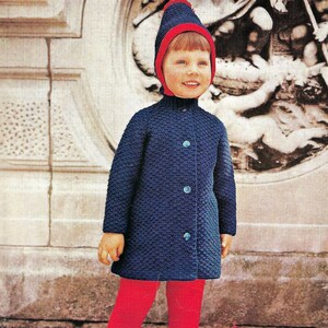 May include: A child wearing a blue knitted coat with red trim, red trousers, and black shoes. The child is wearing a red and blue knitted hat.