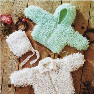 May include: Two knitted baby jackets, one white with a speckled pattern and one light green, with a matching white knitted hat with a speckled pattern.
