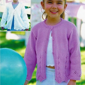 Peut inclure: Une jeune fille portant un cardigan en tricot de couleur mauve clair avec une fermeture boutonnée et un ourlet festonné. Le cardigan présente un délicat motif de dentelle sur le devant et les manches. La fille tient un ballon turquoise.