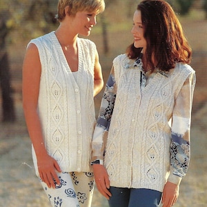 May include: Two women wearing cream-coloured, sleeveless, button-down knit vests with a diamond pattern. One woman wears the vest over patterned trousers, and the other over a patterned blouse and blue trousers. The background is a blurred outdoor scene.