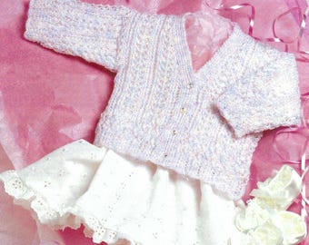 May include: A long-sleeved, V-neck cardigan knitted in a variegated pastel yarn of white, pink, and blue, featuring a textured cable pattern and small buttons. It is paired with a white skirt with eyelet lace detailing and matching white shoes.