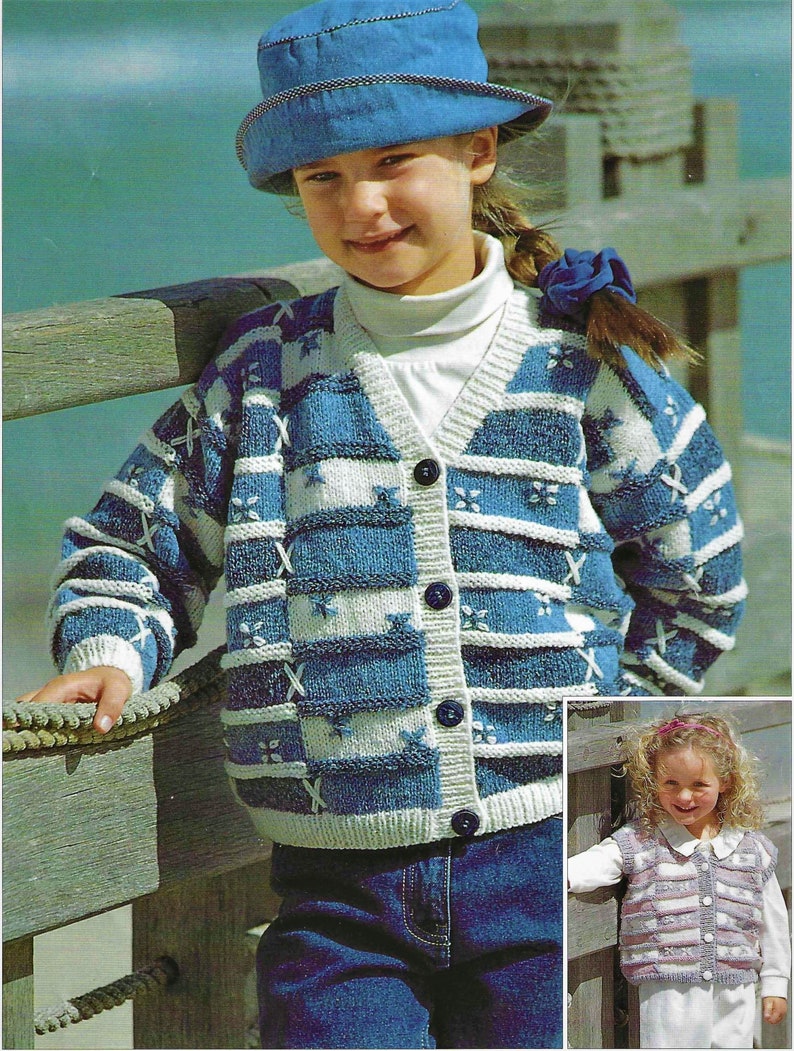 Pu&ograve; includere: Due bambini indossano cardigan di lana. La bambina a sinistra indossa un cardigan a righe blu e bianche con un motivo a stella. La bambina a destra indossa un cardigan a righe rosa e bianche. Entrambi i cardigan hanno bottoni sul davanti.