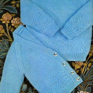 May include: Two light blue knitted sweaters, one with buttons, laid out on a floral patterned fabric.