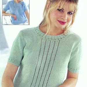 Puede incluir: Una camiseta de punto verde claro de manga corta con cuello redondo y detalles calados verticales en la parte delantera. La camiseta tiene un aspecto delicado y texturizado. Una imagen más pequeña de una camiseta azul similar está en la esquina superior izquierda.