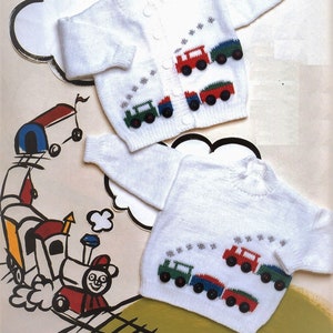 May include: Two white knitted baby cardigans with a train design. The cardigans feature a green, red, and blue train with white smoke and stars. The cardigans are buttoned up the front.