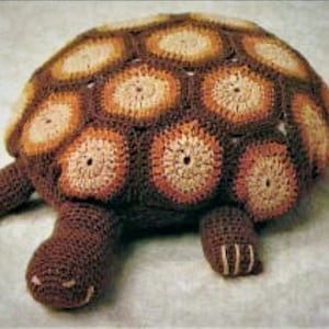 May include: A crocheted turtle toy with a brown shell and tan accents. The shell is made of multiple circular crocheted pieces.