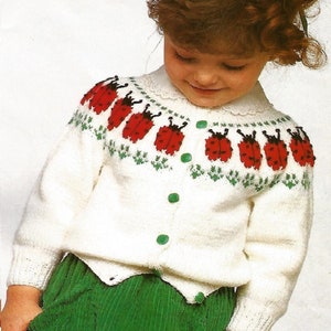 May include: A white knitted cardigan with a green and red ladybug pattern on the neckline. The cardigan has a button closure and long sleeves.