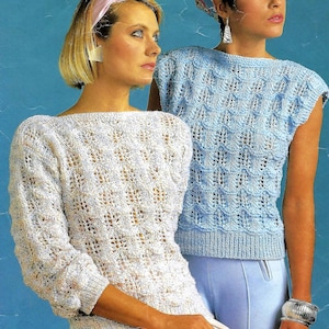 May include: Two women wearing crocheted sweaters. The woman on the left is wearing a white sweater with a light blue and white pattern. The woman on the right is wearing a light blue sweater with a white pattern. Both sweaters have a loose, open weave.