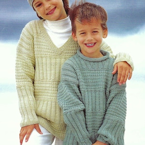 Könnte beinhalten: Zwei Kinder in handgestrickten Pullovern. Eines trägt einen hellgrünen Pullover mit V-Ausschnitt und eine gestreifte Mütze. Das andere trägt einen blau-grünen Pullover mit Rundhalsausschnitt. Die Pullover haben ein strukturiertes Rippendesign.