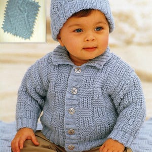 以下が含まれることがあります： ボタン留めのライトブルーのニットベビーカーディガンと帽子。カーディガンはテクスチャのあるステッチパターンで、帽子にはポンポンが付いています。