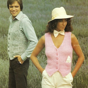 May include: Two people wearing knitted vests, one in a light gray vest and the other in a pink vest. The person in the pink vest is wearing a white hat and a white bow tie.