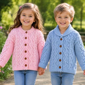 May include: A light pink cable-knit cardigan with a round neckline and brown buttons, and a light blue cable-knit cardigan with a shawl collar and brown buttons. Both garments feature intricate textured patterns and long sleeves, worn with blue jeans.